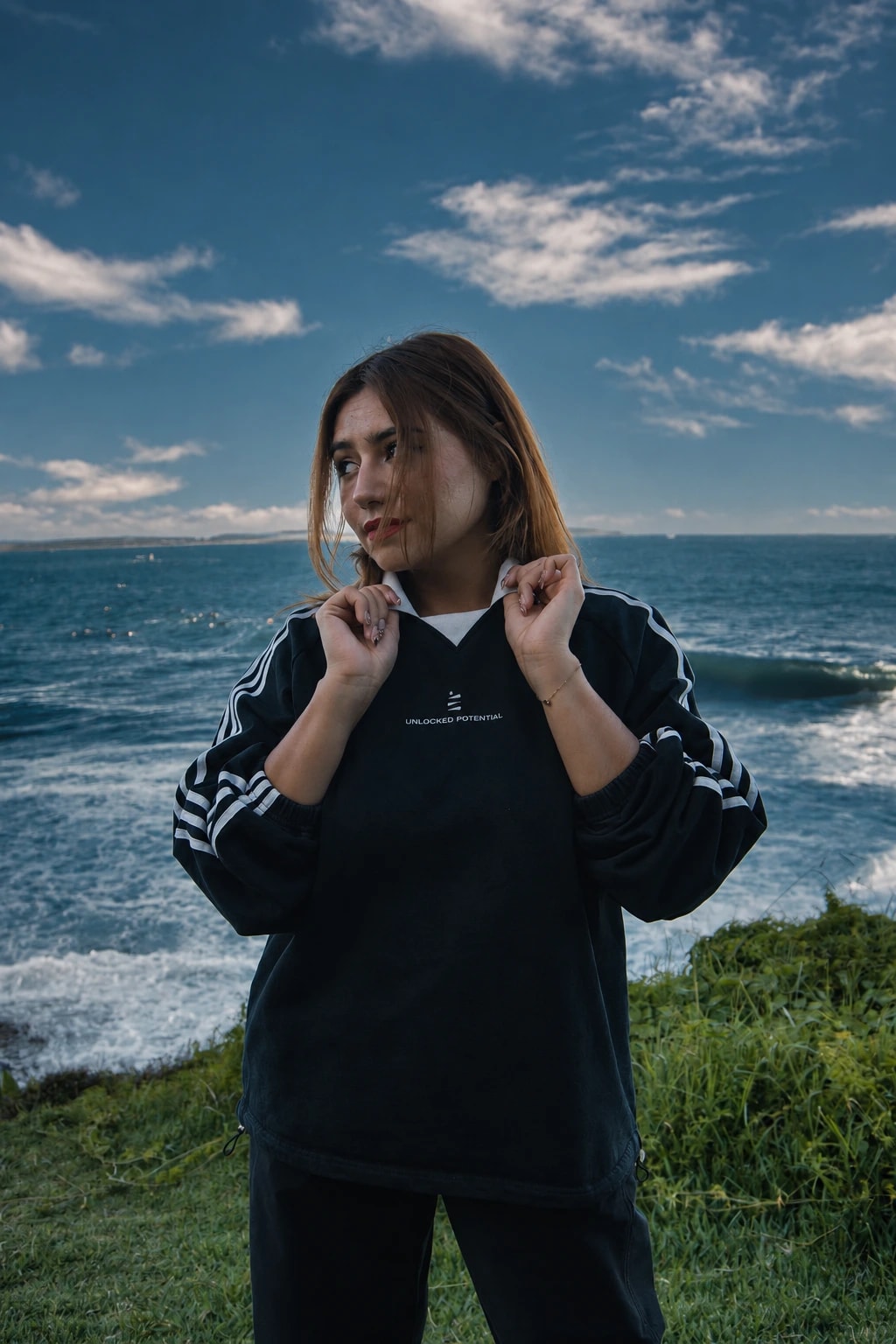 Mayte sujetando el cuello de su jersey DIV3NITY junto al mar